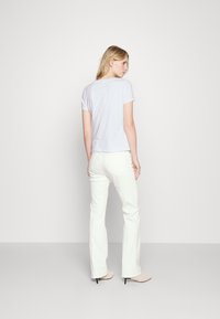 Camiseta de color púrpura claro con mangas cortas, combinada con pantalones vaqueros acampanados blancos. El material parece suave con un diseño ajustado y escote sutil.