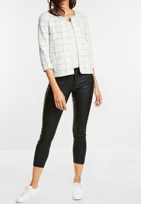 Vit och grå rutig kort jacka med trekvartsärmar, tillsammans med svarta snugga byxor och vita sneakers. Enkel rund krage.