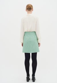Hvid langærmet bluse med puffede ærmer, parret med en grøn tweed mini nederdel, sorte tights og kraftige sorte hæle.