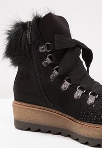 Bottine en daim noir avec semelle épaisse à crampons, larges lacets en ruban, fermeture éclair latérale, œillets métalliques et bordure en fourrure noire au col.