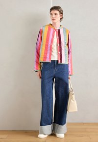 Bunte, gestreifte, steppte Jacke mit rundem Kragen, Knopfverschluss und weit geschnittenen Jeanshosen, kombiniert mit einer hellen Handtasche und weißen Schuhen.