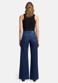 Jeansy dżinsowe z wysokim stanem i szerokimi nogawkami w ciemnoniebieskim kolorze. Posiadają cztery tylne kieszenie oraz surowe brzegi dla casualowego wyglądu.