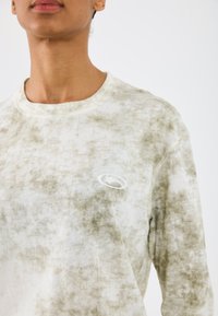 Jasnozielony sweatshirt w tie-dye z okrągłym dekoltem, z małym białym logo na piersi. Miękki materiał o teksturowanym wykończeniu.