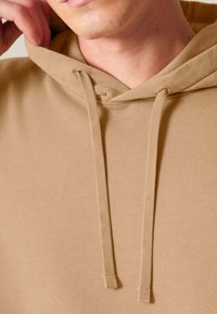 Svetlohnedá mikina s kapucňou, hladkou štruktúrou, s vreckom typu kangaroo a sťahovacími šnúrkami.