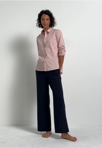 Camicia a righe rosa chiaro con bottoni abbinata a pantaloni larghi blu navy. La camicia ha maniche lunghe e una vestibilità rilassata, con bottoni visibili e colletto.