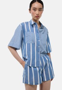 Chemise à manches courtes rayée bleue et blanche avec deux poches poitrine et un short assorti, fabriquée en tissu léger.