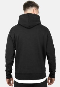 Felpa nera con tasca a marsupio, cappuccio con cordino, polsini e orlo a costine, caratterizzata da una texture liscia e un design minimalista.