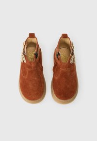Scarpe per bambini in suede marrone con zip laterali e applicazioni di fiori beige, viste dall'alto su uno sfondo bianco.