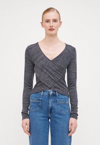 Haut à manches longues gris foncé avec un col en V, présentant un design enroulé et une texture côtelée, associé à un jean en denim bleu taille haute.