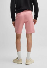 Pantalones cortos de color rosa claro hechos de algodón, con dos bolsillos traseros y dobladillos enrollados, combinados con una camiseta de manga larga negra y zapatillas crema.