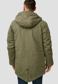 Olivengrønn hetteparka med teksturert overflate, med et diamantlogo på hetten og en knappedetalj bak i kanten.
