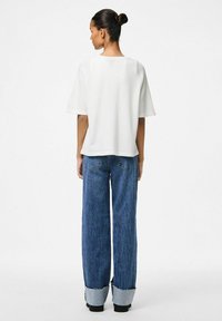 Balta īsām piedurknēm blūze ar brīvu piegriezumu, apvienota ar platām kājām zila denima džinsiem ar neapstrādātu apakšmalu un aizmugures kabatām.