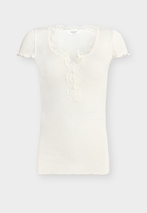 Fehér bordázott rövid ujjú felső hullámos szegéllyel, csipkével díszített V-nyakkivágással és három apró gombbal az elején.