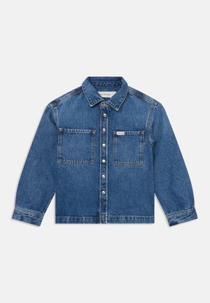 Denimjakke i middels blå med krage, frontknapplukking og to brystlommer. Har store sømmer og en avslappet passform.