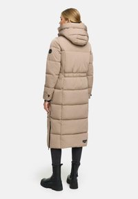 Piumino lungo beige con colletto alto e cappuccio, caratterizzato da sezioni trapuntate orizzontali e cerniere laterali per una vestibilità regolabile. Accentatura con etichetta nera.