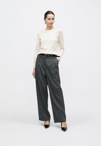 Top manica lunga color beige chiaro, pantaloni plissettati grigi, cintura nera e tacchi neri appuntiti. Tessuto liscio e vestibilità su misura.