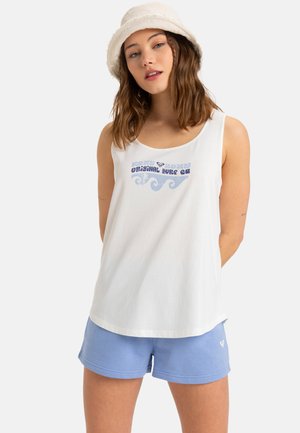 Hvid tanktop med blå grafisk tekst og bølgemønster, parret med lyseblå bomuldsshorts. Modellen bærer en blød, cremet farvet bucket hat.