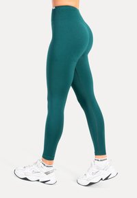Leggings taille haute couleur sarcelle en matière extensible avec une texture lisse. Présentent une couture discrète le long des côtés et une ceinture à logo.