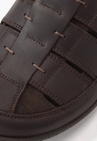 Braune Leder-Sandale mit einem gewebten Design, gestickten Akzenten und Ausschnitten. Weiche Textur mit einem strukturierten Sohlenrand.