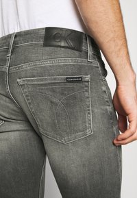 Grå denimjeans med en smal passform, med tydliga bakfickor och en svart läderetikett i midjan med präglad branding.