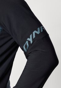 Fekete sportos hosszú ujjú póló sima textúrával. A felső karon kék "DYNA" logó található, és testhezálló fazonú.