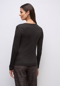 Tmavě hnědý top s dlouhými rukávy a kulatým výstřihem, hladká textura, spárovaný s hnědými kalhotami s jemným vzorem pruhů.