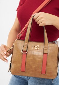 Sac à main en simili-crocodile tan avec des accents rouges, doubles anses supérieures et une bandoulière détachable. Détail du logo doré sur le devant.