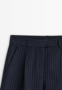 Navy pinstriped trousers with a textured fabric, featuring a structured waistband, side pockets, and subtle contrasting stitching.