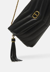 Borsa a tracolla in pelle nera con motivo trapuntato, accessori in metallo color oro e un tassello come dettaglio. Presenta una tracolla in catena per versatilità.