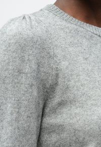 Pulover gri din tricot are un decolteu rotunjit și umeri puțin puffiți, prezentând o textură moale și un design ușor.