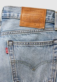 Poche arrière de jean en denim bleu clair avec étiquette en cuir marron Levi Strauss & Co. et étiquette rouge Levi's sur la couture de la poche.