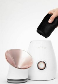 Ansiktsångmaskin med en glänsande design i roséguld och vitt; inkluderar en svart handduk, oval ångkon och kontrollratt med märkta inställningar.