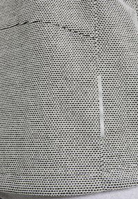 Texturiertes Gewebe in Schwarz und Weiß mit einem Karomuster und einem hellgrauen Akzentstreifen. Die Nahtdetails sind entlang der Nähte sichtbar.