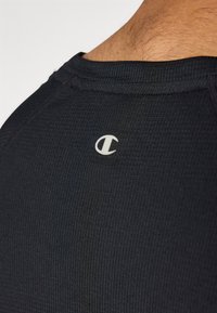 Schwarzes Sportshirt aus strukturiertem Stoff, mit einem kleinen weißen Logo am Nacken und einem gerippten Kragendesign.