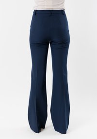 Pantaloni a zampa d'elefante blu navy realizzati in tessuto morbido con vita alta, dotati di passanti per cintura, due tasche posteriori e una vestibilità sartoriale.
