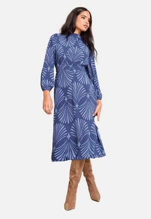 Navyblaues Midikleid mit einem Blattformmuster, das einen hohen Kragen, Ballonärmel und eine taillierte Taille aufweist. Kombiniert mit tanfarbenen Wildleder-Stiefeln, die bis zum Knie reichen.