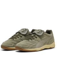 Baskets de sport vert olive en daim avec une semelle épaisse et rembourrée, dotées d'une languette proéminente avec logo et de détails de couture texturée.