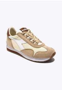 Sneaker beige in suede e tela con accenti bianchi, punta rotonda, lacci testurizzati e suola in gomma marrone. Presenta un logo sulla linguetta.