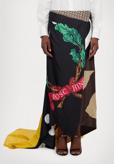 Falda maxi con tejido negro adornado con hojas verdes y una cinta roja, dobladillo asimétrico y detalles amarillos. El material parece suave y ligero.