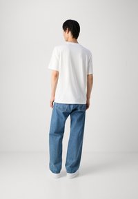 Hvid T-shirt med korte ærmer og rund halsudskæring, parret med lyseblå afslappede jeans. Skoene er hvide med en glat overflade.