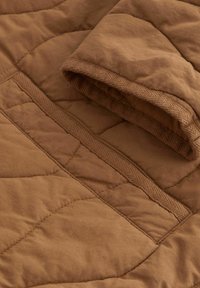 Tissu matelassé brun avec des coutures détaillées et un gros plan d'un bord plié montrant une bordure texturée et des lignes de couture.