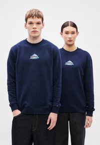 Tengerészkék pulóverek bordázott mandzsettával és szegéllyel, hegyi grafikával és fehér, valamint türkiz "tommy jeans" logóval. Simaszövetes anyag.