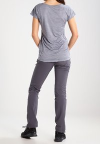 Šedé tričko s krátkým rukávem a mírně volným střihem, kombinované s tmavě šedými elastickými kalhotami a černými sportovními botami. Zadní pohled.