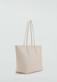Bolso tote beige con textura suave, forma plana y dos asas largas. Presenta un diseño minimalista sin herrajes o adornos visibles.