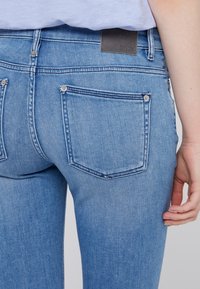 Ljusblå denimjeans med en standard femficksdesign, subtil blekning och en läderetikett sydd vid midjan.