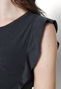 Tmavě šedý krátký rukáv top s volánkovým detailem na rameni. Měkká, lehká tkanina s hladkým povrchem. Jednoduchý, čistý výstřih.