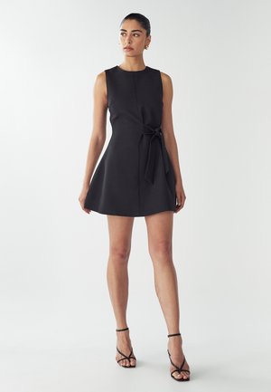 Black sleeveless dress with a fitted bodice and flared skirt, featuring a tied waist detail. Made from smooth fabric with minimal seams.