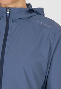 Giubbotto a vento azzurro chiaro con zip frontale, cappuccio regolabile e logo "ENDURANCE". Realizzato in materiale liscio e leggero.