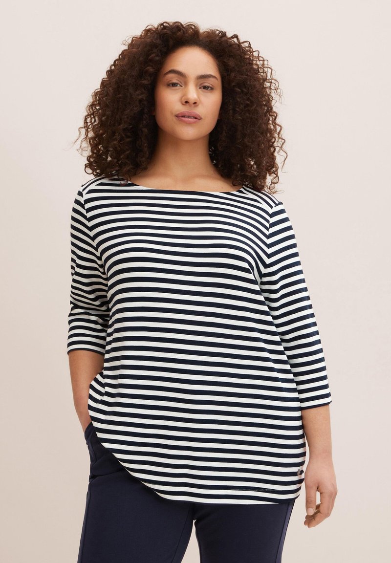 Schwarz-weiß gestreiftes Langarmshirt mit Bootsausschnitt und lockerer Passform, kombiniert mit dunklen Marinehosen.