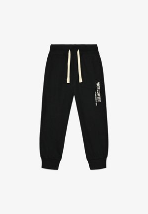 Czarne spodnie dresowe wykonane z bawełny, z sznurkowym paskiem w talii i elastycznymi mankietami. Na lewej nogawce biały napis "WORLDWIDE".